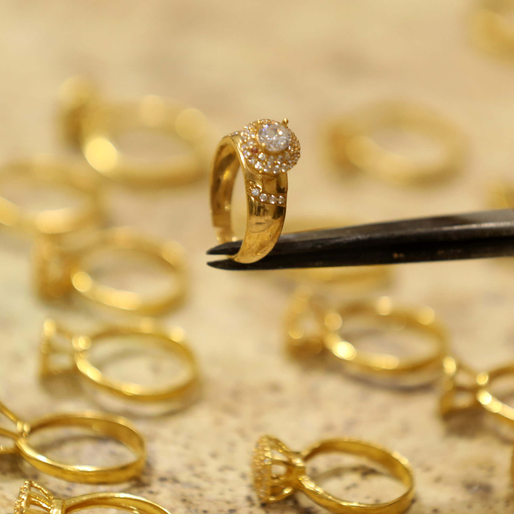 A gold ring being held with pliers over other gold rings.